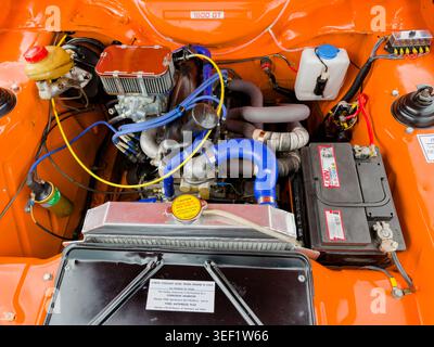 High angle close up under bonnet view of a modified Ford Escort 1600 GT engine bay with orange paint and chrome components Stock Photo