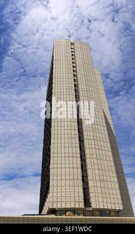 Modern office building reaching high into a bright blue sky filled with white patchy clouds, representing urban development, business, and contemporar Stock Photo