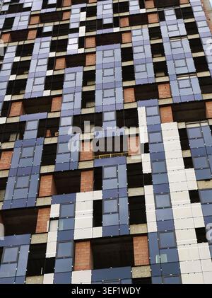 Modern skyscraper exterior showing a textured geometric pattern of blue reflective glass panels, white segments, and exposed brick walls, symbolizing Stock Photo