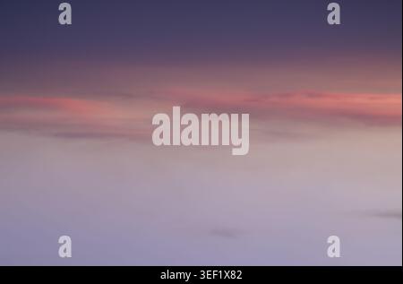 The evening sky in a seamless gradient of twilight hues, where deep indigo dissolves into a soft, ethereal lavender. Wisps of coral-tinted clouds drif Stock Photo