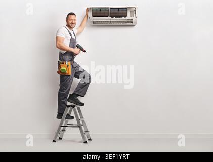 Air conditioning technician on a ladder repairing an indoor AC unit Stock Photo