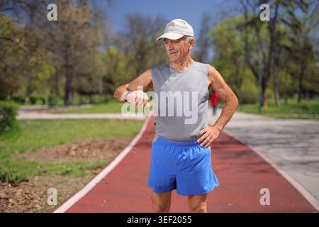 Elderly man in sportswear checking his smartwatch on a running track Stock Photo