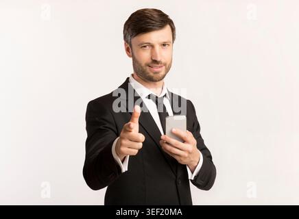 Business Professional Smiling and Using Smartphone While Pointing Towards the Camera Stock Photo