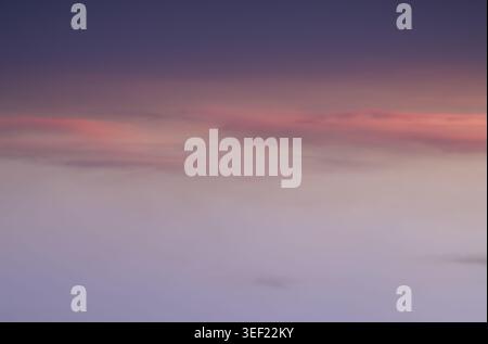 The evening sky in a seamless gradient of twilight hues, where deep indigo dissolves into a soft, ethereal lavender. Wisps of coral-tinted clouds drif Stock Photo
