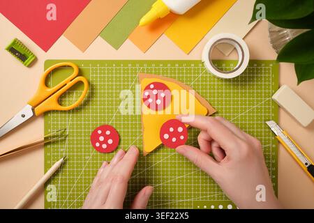 Hands making paper pizza craft with colorful stationery tools on cutting mat. Creative DIY activity, handmade hobby and art project. Stock Photo