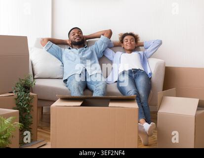 African American Spouses Relaxing Sitting On Couch In New Apartment Stock Photo