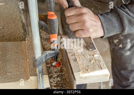 Carpenter hands working with wood clamp and chisel in woodworking workshop Stock Photo