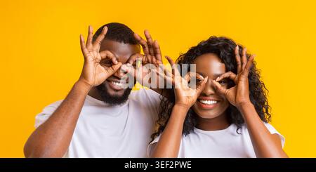 Couple Having Fun and Expressing Joy Against a Bright Yellow Background While Making Hand Signs Stock Photo