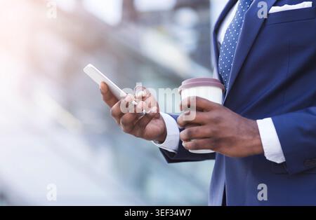 Unrecognizable Businessman Texting On Phone Holding Coffee Standing In City Stock Photo
