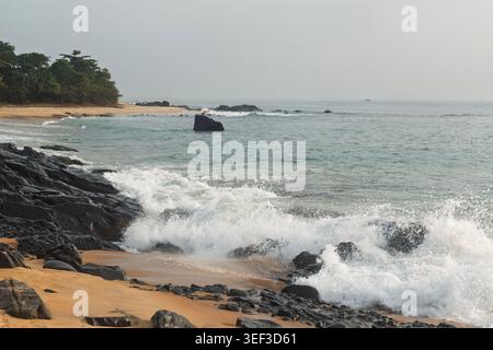Black rocks break the waves on the beach of Robertsport. Liberia, West Africa Stock Photo