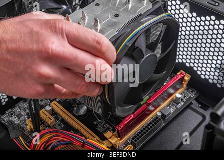 A person's hand is shown installing CPU cooler onto a motherboard inside a desktop computer case. Stock Photo