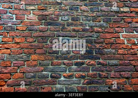 A straight-on close-up view of an authentic aged brick wall featuring a rich multi-colored texture of red, orange, and dark weathered bricks. The roug Stock Photo