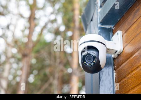 Outdoor security camera mounted on wooden house wall in forest, close surveillance detail. Concept: home security Stock Photo