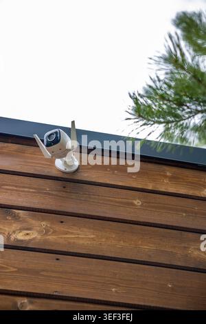 Wireless security camera mounted on wooden cabin exterior in forest, outdoor surveillance detail. Concept: home security Stock Photo