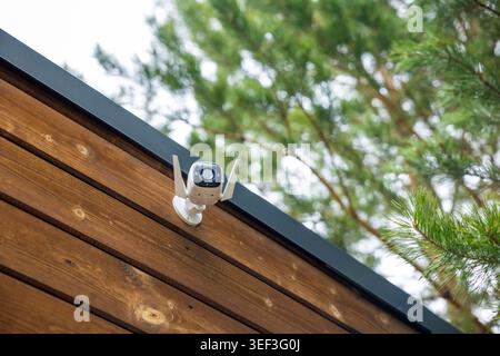 Wireless security camera mounted on wooden cabin exterior in forest, outdoor surveillance detail. Concept: home security Stock Photo