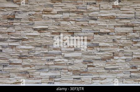 Stone paneling wall made of reconstructed rock of beige, off white and gray colors. Panels for exterior. Background and texture. Full frame. Stock Photo