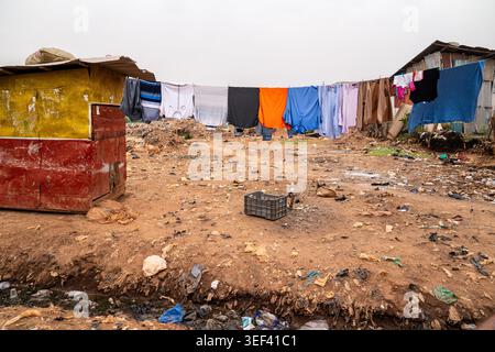 A long clothesline with colorful garments crosses an arid ground polluted with waste in Arua, Uganda. Makeshift wood and iron shacks stand on both sid Stock Photo