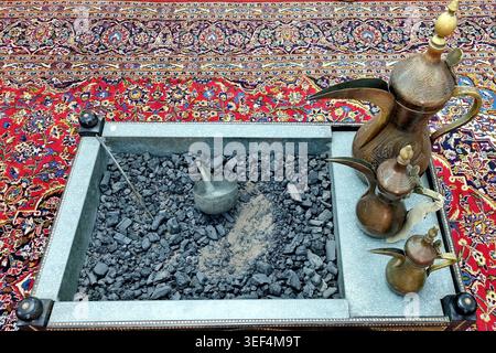 Ornate coffee-making setup in an Oriental context, featuring a metal tray filled with hot coals, placed on a richly patterned red and blue rug Stock Photo