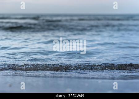 Small bubbles of sea foam on wet sand. Calm sea on the horizon line. Stock Photo
