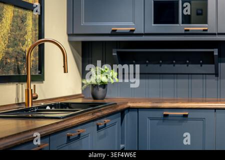 Modern blue kitchen with copper faucet. Stylish interior featuring wooden countertop and decor. Stock Photo