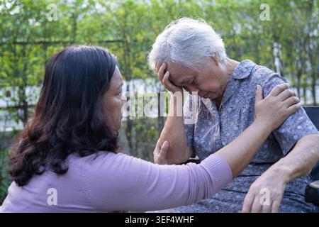Asian elderly woman headache while sitting on wheelchair at park, healthy strong medical concept. Stock Photo
