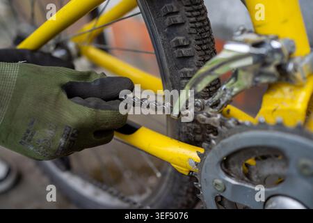 Close up volunteer adjusting derailleur and chain on yellow bicycle, gloved hands using pliers to align gears, Stock Photo