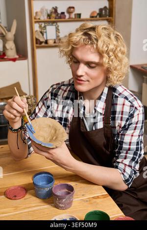 Blonde artisan skillfully shapes clay into art while enjoying the creative atmosphere. Stock Photo