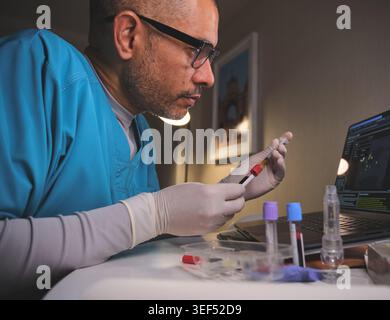 Scientist analyzing blood sample data on a laptop in a medical research laboratory Stock Photo