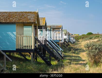 Row of colorful traditional wooden beach huts raised on stilts along the grassy sand dunes at Hunstanton, Norfolk, England Stock Photo