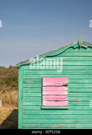 Close-up profile view of a green painted wooden beach hut with contrasting pink window shutters at Hunstanton, Norfolk, England Stock Photo