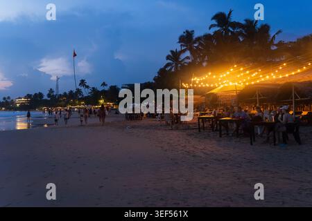 MIRISSA, SRI LANKA - Tourists dine at candlelit tables on Mirissa Beach at dusk. Stock Photo