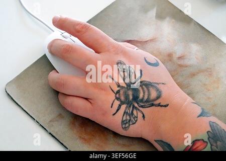 A bee tatoo on a young woman working a computer mouse on a mouse pad in an office in Bend, Oregon. Stock Photo