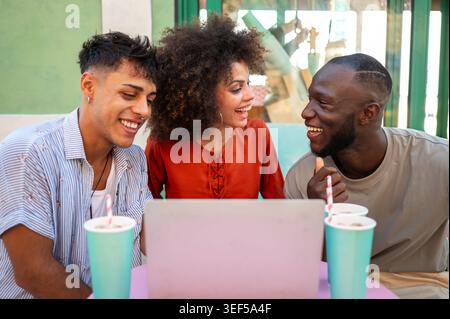 Students gather for a friendly cafe study session, learning together with a laptop, discussing ideas Stock Photo