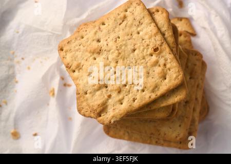 stack of square brown whole grain crackers on white paper, crunchy biscuit texture, top view with soft focus, healthy snack and culinary Stock Photo