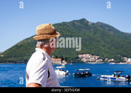 Man with straw hat walks seaside and looking at boats on sea in Perast, Montenegro Stock Photo