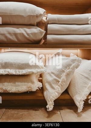 Neutral linen pillows and folded blankets on wooden shelves, cozy home textile display with natural textures and warm minimalist decor Stock Photo