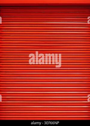 Red shutter door with horizontal pattern and strong color impact. Front view with clear geometry and urban context. Copy space. Stock Photo