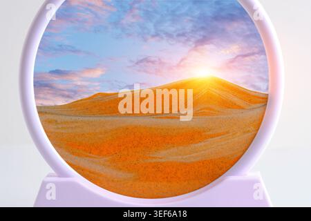Circular kinetic sand art depicting glowing sunset over orange desert dunes under cloudy sky Stock Photo