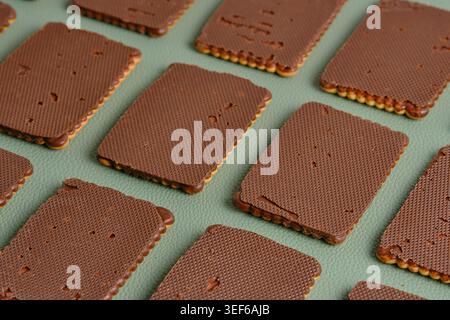 Angled close up dark chocolate glazed biscuits organized on green leather like texture Stock Photo