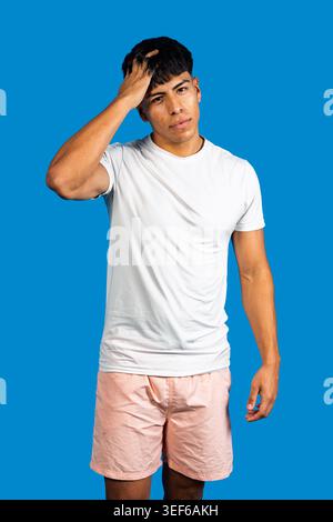 Young man scratching head feeling confused or having a problem on blue background Stock Photo
