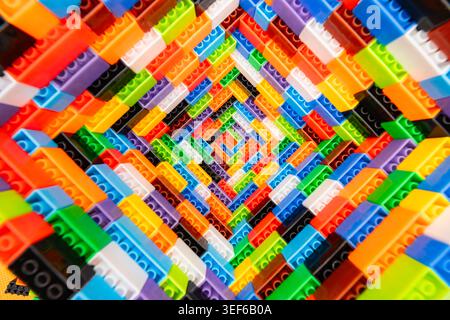 Abstract colorful background pattern made of plastic toy building blocks stacked in a deep spiral tunnel shape close up Stock Photo