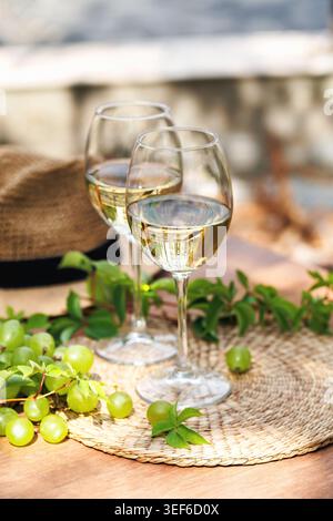 White Wine Glasses with Grapes and Straw Hat on Table Stock Photo
