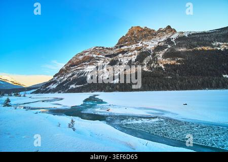 Snowy Mountain Peak Frozen River and Dense Evergreen Forest in Winter Stock Photo