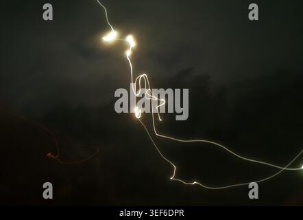 Light trails capturing motion during a long exposure in an abstract composition, showcasing the dynamic movement of light against a dark, cloudy night Stock Photo