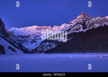 Winter Sunrise Over Frozen Lake With Snow Covered Mountains And Forest Stock Photo