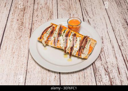 Long toast topped with tomato, anchovy and white fish fillets served with orange dipping sauce on white plate over wood Stock Photo