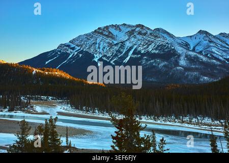 Snow Covered Mountain River and Evergreen Forest at Sunrise in Winter Stock Photo
