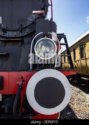 Close-up view of a vintage steam locomotive front featuring a prominent headlight, circular buffer and weathered metal textures. Evokes nostalgia, ind Stock Photo