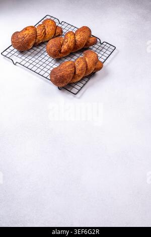 Three braided cinnamon sugar sweet rolls, golden brown and freshly baked, cooling on a black wire rack ready for breakfast or a cozy snack Stock Photo