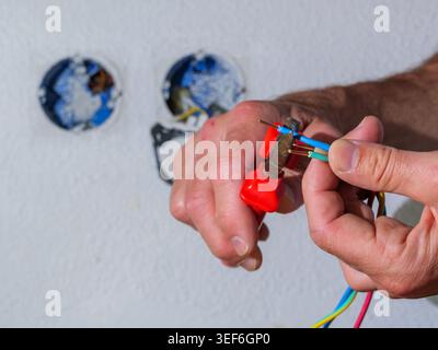 Cutting electrical wires during home installation work. Close-up of hands using tool while working with electrical cables. Stock Photo